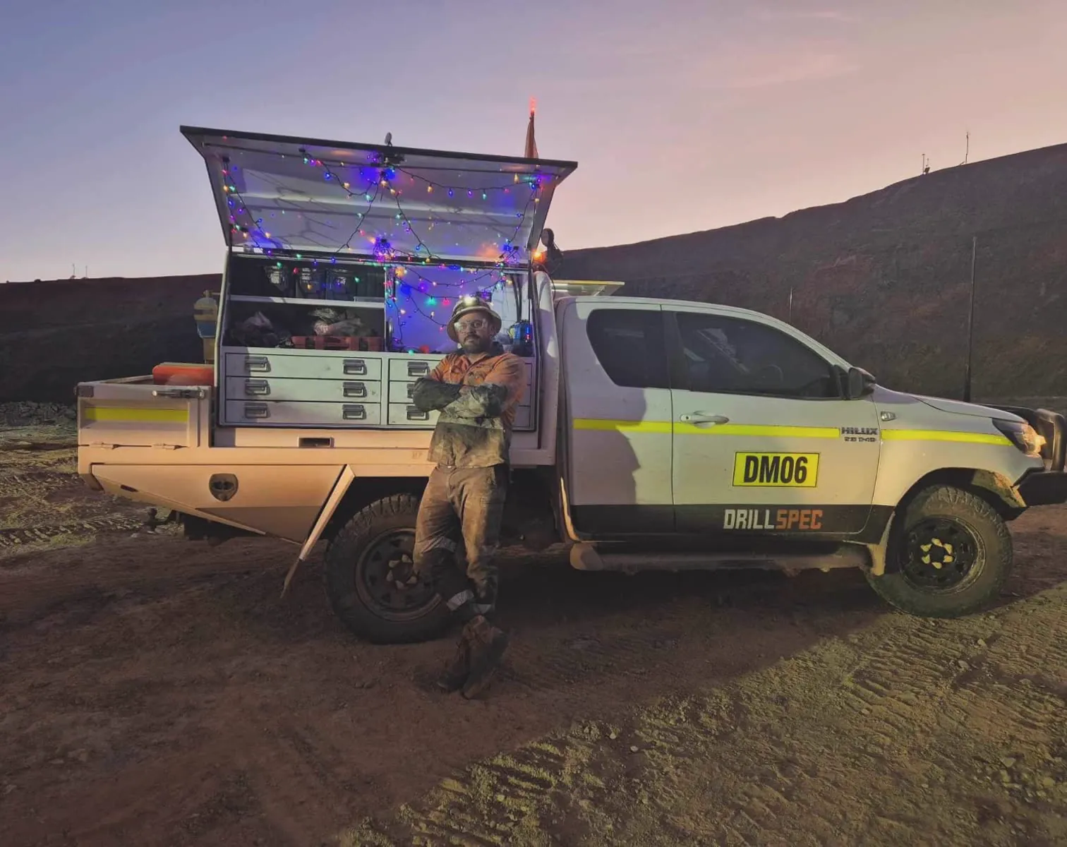 Drillspec DM06 ute with its canopy strung in Christmas lights at dusk, tech leaning on the tray