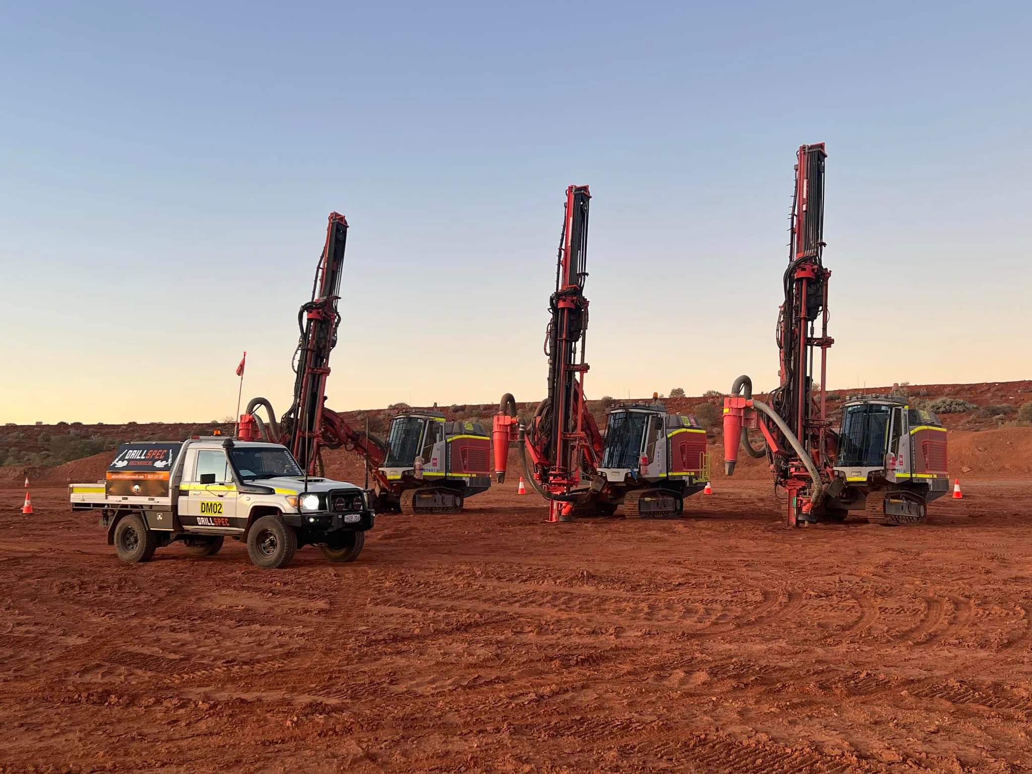 Drillspec DM02 service ute with three production drill rigs lined up at sunset
