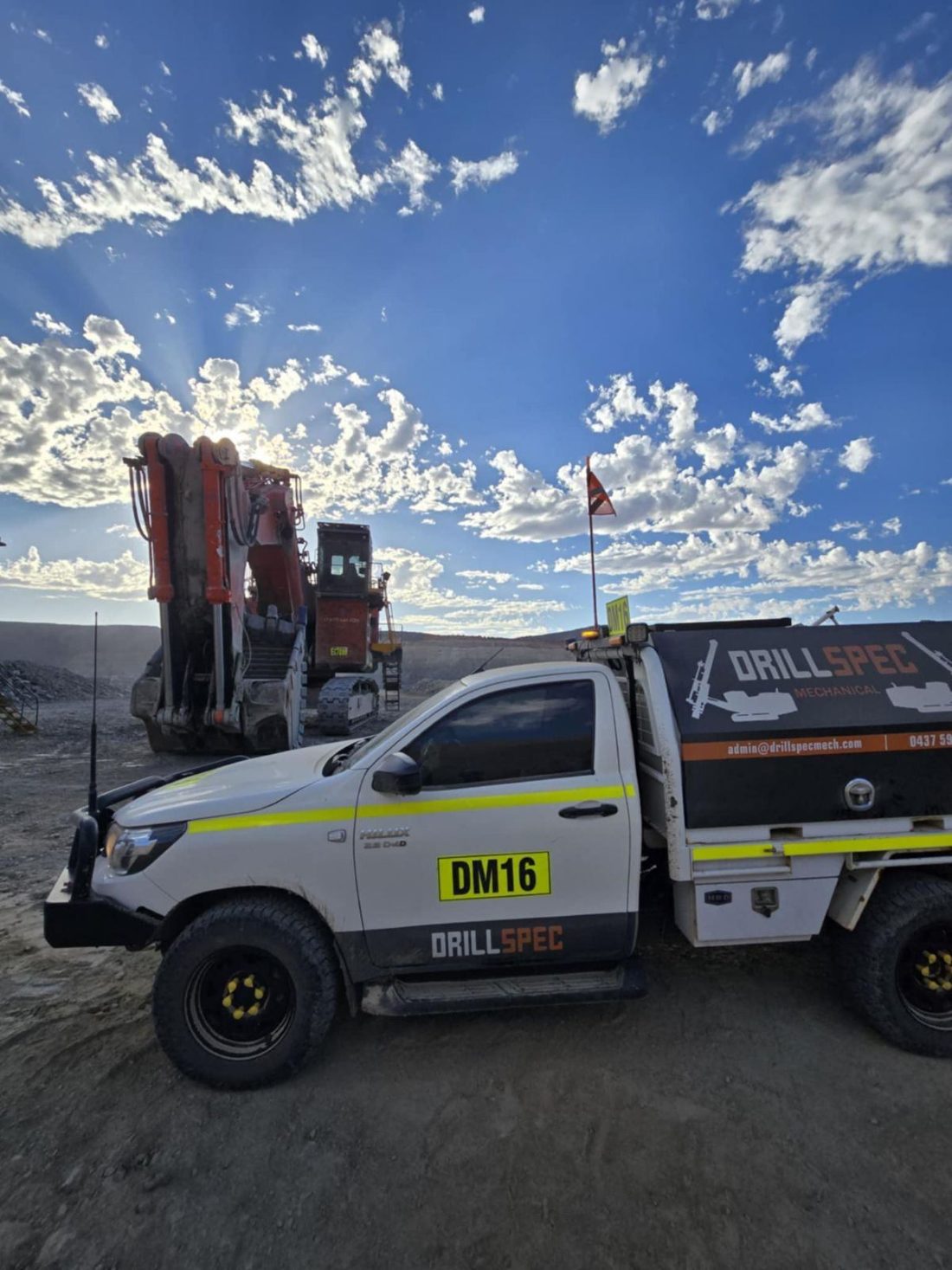 Drillspec DM16 ute beside a tracked excavator at sunrise