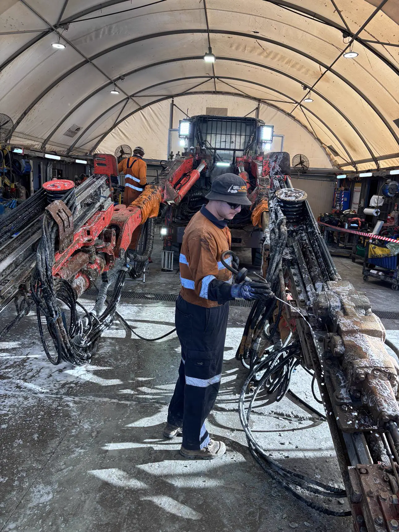 Drillspec technician in branded gear washing down an underground jumbo drill rig at the washbay
